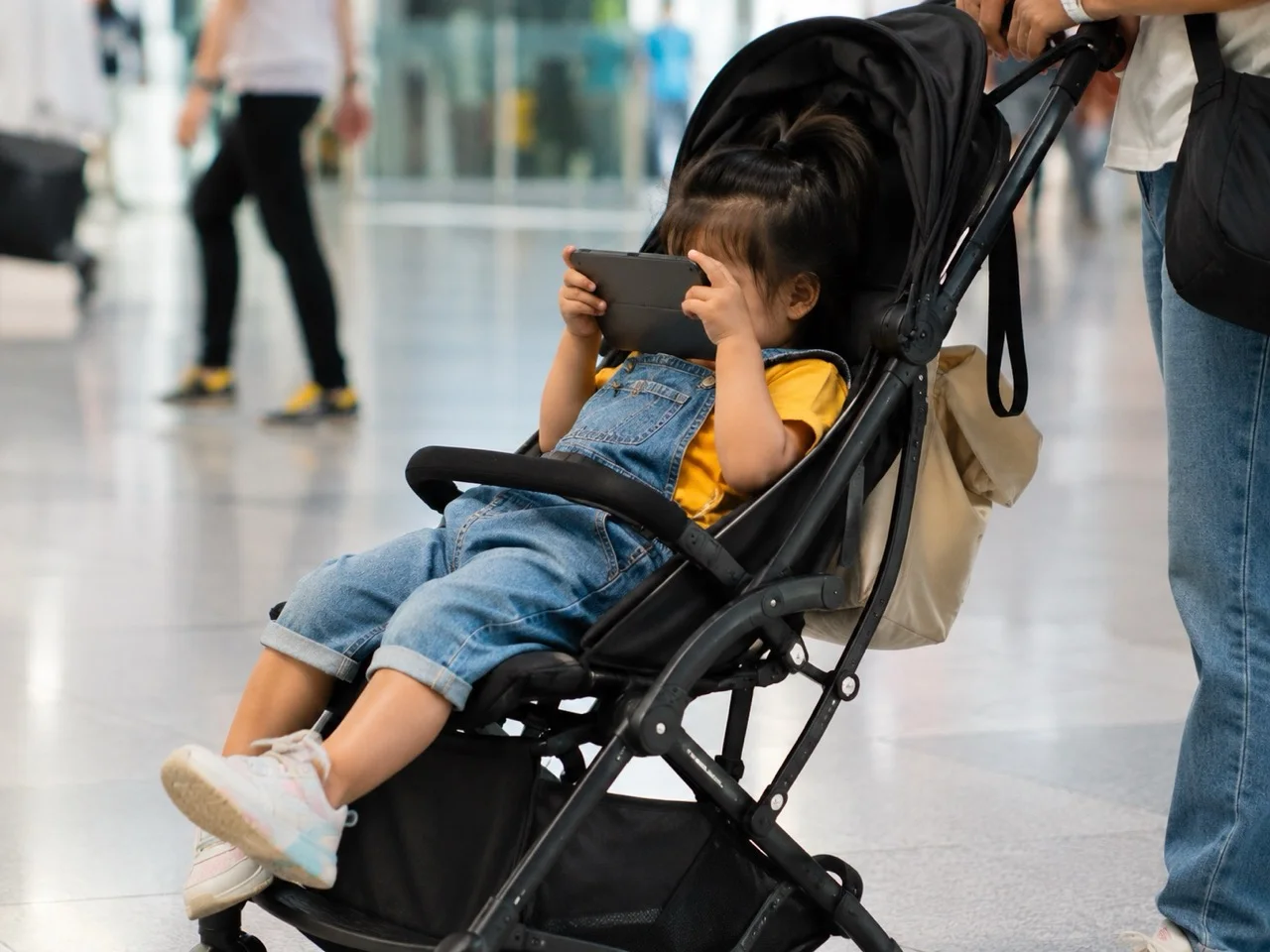 A young child watching a phone in a stroller, illustrating the choice between screen time and real-world activity