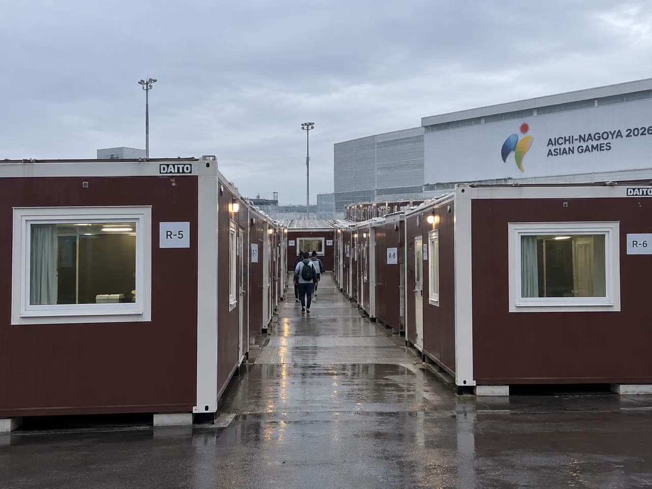 Container-style temporary accommodation at Nagoya Port, with DAITO units numbered R-5, R-6 and R-8 in front of an Asian Games building