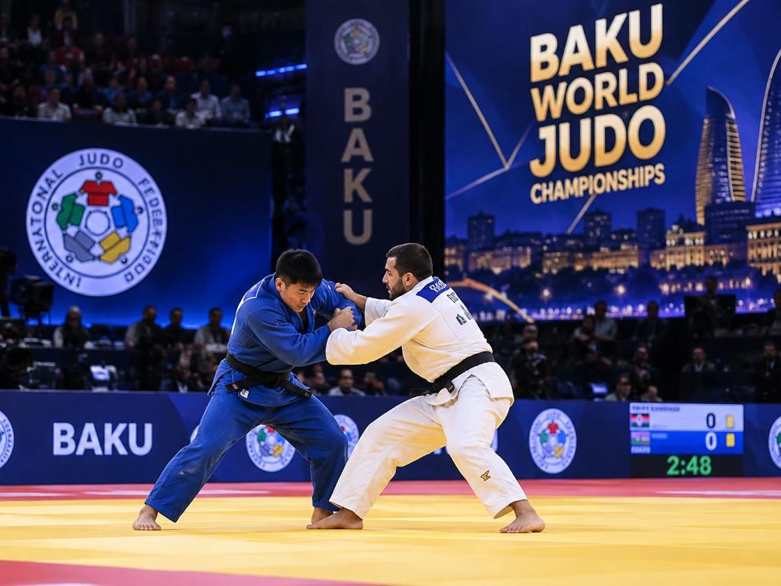 Two judoka contesting on the mat with the scoreboard alongside